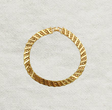 Load image into Gallery viewer, Gold-plated brass bracelet featuring wide angled links with a textured diagonal pattern, displayed in a circular shape on a soft white textured background. 