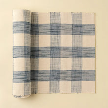 Load image into Gallery viewer, Blue-and-cream gingham table runner partially unrolled on a cream background. 