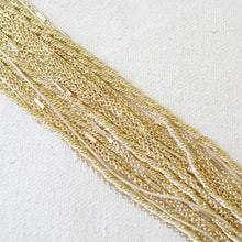 Load image into Gallery viewer, Close-up of a gold-plated multi-strand chain bracelet featuring mixed chain styles, including cable, curb, and snake chains, displayed on a textured white surface.  