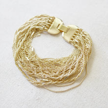 Load image into Gallery viewer, Gold-plated brass multi-strand chain bracelet with a wide clasp displayed on a textured white surface. 
