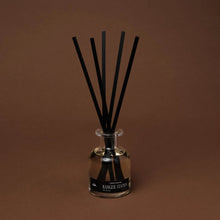 Load image into Gallery viewer, Ranger Station Cowboy Christmas reed diffuser in a reflective glass bottle with black reeds fanned out, displayed against a warm brown background.