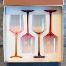 Load image into Gallery viewer, Set of four hand-blown crystal wine glasses with gradient stems and bases in amber, rose, plum, and red tones, displayed in a white fitted foam insert inside of an open gift box on a wooden surface. 