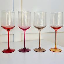 Load image into Gallery viewer, Set of four hand-blown crystal wine glasses with gradient stems and bases in red, plum, amber, and rose, arranged in a row on a white surface against a white background.  