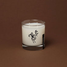 Load image into Gallery viewer, Ranger Station Cowboy Christmas candle with double wicks in a clear glass jar featuring a black cowboy illustration, displayed against a warm brown background. 