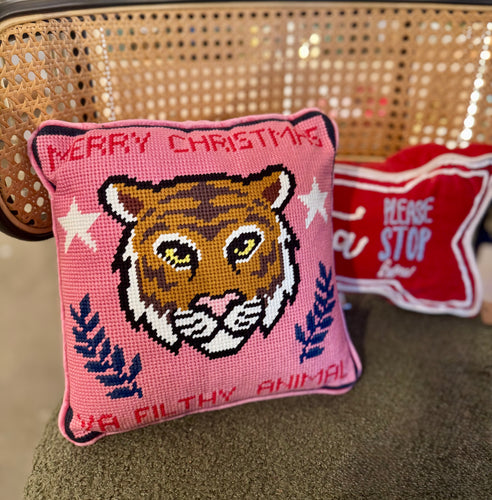 Pink needlepoint pillow featuring an orange tiger face with yellow eyes and a pink nose, white stars, and navy botanical motifs, with 