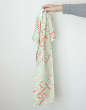 Load image into Gallery viewer, Cotton kitchen towel with a mint-green background and a red and cream candy cane pattern, shown hanging from a hand against a white background.