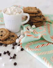 Load image into Gallery viewer, Cotton kitchen towel with a mint-green background and a red and cream candy cane pattern styled on a white surface with a white mug of hot cocoa topped with marshmallows, stacked chocolate chip cookies, scattered chocolate chips and marshmallows. 