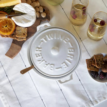 Load image into Gallery viewer, White stoneware brie baker with matching lid and handles, shown from above on a table setting with cheese, crackers, fruit, nuts, and two glasses. 