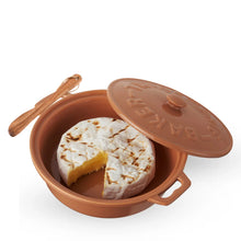 Load image into Gallery viewer, Terracotta-colored stoneware brie baker holding baked brie with a wedge removed, shown with the matching lid resting on top and a wooden spreader on a handle. 