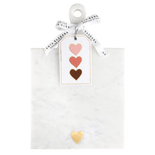 Load image into Gallery viewer, White marble serving board with a brass heart inlay and decorative heart gift tag, displayed on a white background. 