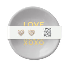 Load image into Gallery viewer, Small round ceramic ring dish with gold text paired with gold-plated heart stud earrings with pavé-set clear stones. 