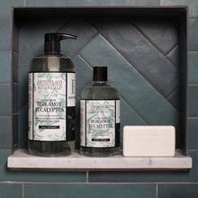 Load image into Gallery viewer, Archipelago Botanicals Bergamot Eucalyptus body wash in a large clear pump bottle and a smaller screw-cap bottle displayed in a teal tiled shower niche with a white bar soap. 