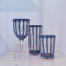 Load image into Gallery viewer, Villa BPA-free acrylic cups including wine glass, tall tumbler, and old fashioned cup in a blue denim hue with clear vertical ribbed design on a marble surface.