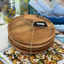 Load image into Gallery viewer, Acacia Plate Set of four round acacia wood plates stacked and tied with twine with tag product label, resting on an open book against a styled background.