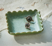 Load image into Gallery viewer, Light green ceramic square trinket dish with scalloped edges and reactive glaze, styled with jewelry on a neutral surface. 