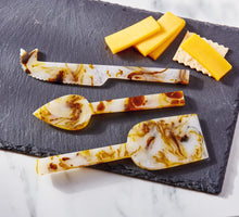 Load image into Gallery viewer, Tortoise Resin Cheese Utensil Set three stainless steel utensils with tortoise shell resin design in ivory, brown, and amber tones including spreader, fork, and knife, displayed on a slate board with sliced cheese and cracker on white marble surface. 