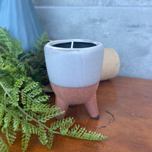 Load image into Gallery viewer, Footed Citro Candle Pot rustic terracotta with gray upper half and brown bottom, hand poured citronella candle, single wick in three leg footed pot on wooden surface with greenery. 