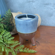 Load image into Gallery viewer, Footed Citro Candle Pot rustic terracotta with blue upper half and brown bottom, hand poured citronella candle with single wick in three leg footed pot on wooden surface with greenery. 