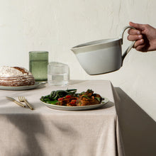 Load image into Gallery viewer, Aquarius Sage stoneware gravy boat with reactive glaze, curved handle, and spout, shown pouring above plated food on a table setting. 