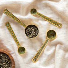 Load image into Gallery viewer, Brio enameled steel measuring spoons with green and gold block leaf pattern and matte gold finish, set of four, displayed on white fabric.