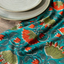 Load image into Gallery viewer, Allure Block Print Dishtowel, cotton towel with hand block-printed floral pattern in coral and olive on a teal background, shown draped on a wooden surface with stacked plates. 