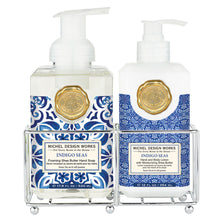 Load image into Gallery viewer, Michel Design Works Indigo Sea foaming shea butter hand soap and hand and body lotion set in clear and white pump bottles, the hand soap featuring a blue and white tile-inspired pattern and the lotion featuring a blue and white medallion pattern, both with gold seal accents, displayed in a double compartment metal caddy on a white background. 