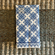 Load image into Gallery viewer, Michel Design Works Indigo Seas hostess napkins in packaging featuring a blue and white tile-inspired pattern with decorative border, displayed on a woven surface. 
