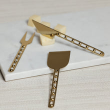 Load image into Gallery viewer, Zodax Córdoba cheese knife set of three in gold-tone stainless steel with beaded handle detail, displayed on white marble board with cheese cubes. 