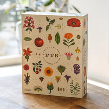 Load image into Gallery viewer, Plant the Box Votive Gift Set, KOBO illustrated botanical gift box with multicolored flowers, leaves, and fruit, displayed closed on wooden surface against soft indoor background. 