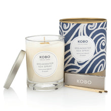 Load image into Gallery viewer, Breakwater Sea Spray Coastal Candle, KOBO pure soy candle in clear glass jar with cream wax and silver-toned lid resting at the side, blue packaging with white wave-inspired swirl pattern and gold-toned rim and base beside, KOBO gray matchbox and two brown-tipped wooden matches in front, against white background. 