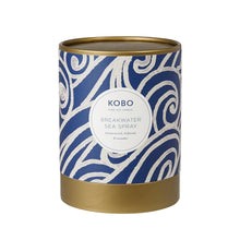 Load image into Gallery viewer, Breakwater Sea Spray Coastal Candle, blue packaging with white wave-inspired swirl pattern and gold-toned rim and base, against white background. 