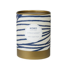 Load image into Gallery viewer, Citrus Sunset Coastal Candle, cream packaging with blue horizontal stripe pattern and gold-toned rim and base, against white background. 