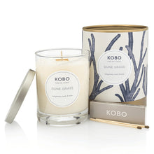 Load image into Gallery viewer, Dune Grass Coastal Candle, KOBO pure soy candle in clear glass jar with cream wax and silver-toned lid resting at the side, cream packaging with blue branch pattern and gold-toned rim and base behind, KOBO gray matchbox and two brown-tipped wooden matches in front, against white background. 