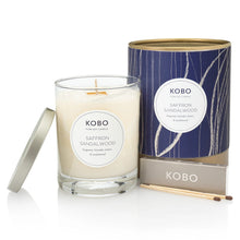 Load image into Gallery viewer, Saffron Sandalwood Coastal Candle,  KOBO pure soy candle in clear glass jar with cream wax and silver-toned lid resting to the side, blue patterned packaging with gold-toned rim and base behind, KOBO gray matchbox and two brown-tipped wooden matches in front, against white background.  