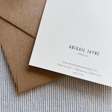 Load image into Gallery viewer, Abigail Jayne card back on white textured paper with brown kraft envelope on gray ribbed fabric surface. 