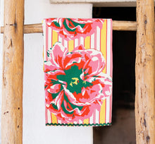 Load image into Gallery viewer, Kitchen Tea Towel, kitchen tea towel with oversized pink, coral, green, and white floral illustrations, yellow and pink striped background, and dark green rickrack trim, displayed hanging on a rustic wooden ladder against a white background. 