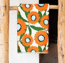 Load image into Gallery viewer, Kitchen Tea Towel, white kitchen tea towel with oversized orange floral prints, green leaves, black accents, and light aqua flower centers and rickrack trim, displayed hanging on a rustic wooden ladder against a white background. 