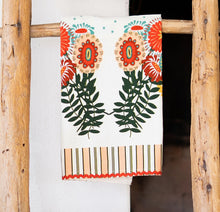Load image into Gallery viewer, Kitchen Tea Towel, white tea towel with orange, teal, and yellow floral illustrations, dark green leafy stems, beige, olive, yellow, and white striped border accents, and orange rickrack trim, displayed hanging on a rustic wooden ladder against a white background. 