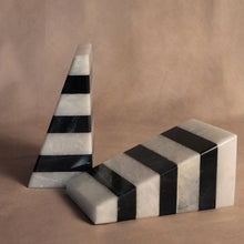 Load image into Gallery viewer, Striped Black &amp; White Marble Bookends, set of hand-shaped, assembled, and polished deep black and white marble triangular wedge-shaped bookends with horizontal striped bands, displayed with one bookend standing upright and the other lying flat on a beige surface and against a coordinating beige background.