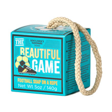 Load image into Gallery viewer, Football Ball Soap On A Rope, square turquoise and black Beautiful Game soap packaging box with white and gold lettering, soccer ball and cleat illustration, and a cream rope extending from the top of the box against a white background. 