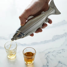 Load image into Gallery viewer, Fish Hip Flask, stainless steel fish-shaped hip flask being used to pour amber liquor into a clear shot glass beside a second filled shot glass on white marble surface. 