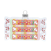 Load image into Gallery viewer, Smarties Candy Ornament, glass ornament resembling three stacked Smarties candy rolls with transparent wrappers revealing pastel rainbow candies, clear twisted ends accented with red glitter dots, a silver-tone hanging cap, and a white hanging ribbon, displayed against a white background. 
