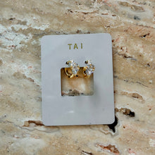 Load image into Gallery viewer, Tiny Triple CZ with Triangle Diamond Huggie, pair of gold-plated hoop earrings with one large triangle-cut and three round cubic zirconia stones arranged in a row displayed on a white TAI jewelry card on a brown stone surface. 