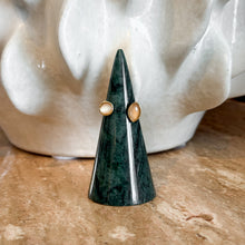 Load image into Gallery viewer, Gold Cats Eye Open Ring, handcrafted open design gold-tone ring with round white and marquise- shaped amber cat's eye bezel-set stones displayed on a dark green marble cone ring holder on a brown stone surface with a white sculpture in background. 