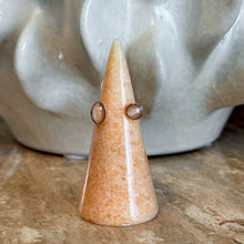 Load image into Gallery viewer, Rose Gold Cat's Eye Open Ring, handcrafted open-design rose gold-tone ring with round and marquise-shaped blush pink cat's eye bezel-set stones displayed on a peach stone cone ring holder on a brown stone surface with white sculpture in the background. 