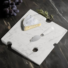 Load image into Gallery viewer, Swiss Cheese Marble Board, hand-polished white marble cheese board with Swiss cheese-inspired cutout details, displayed with a wedge of brie cheese, a mouse-shaped cheese knife with white handle, purple grapes, and rosemary sprigs on a dark marble surface. 