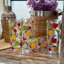 Load image into Gallery viewer, Fresh Pick Drinks Glass Set, set of four clear glass tumblers with colorful fruit illustrations including strawberries, green apples, lemons, orange slices, and blueberries, displayed with a wicker-wrapped stainless steel cocktail shaker and ice bucket with purple flowers on rustic wood surface. 