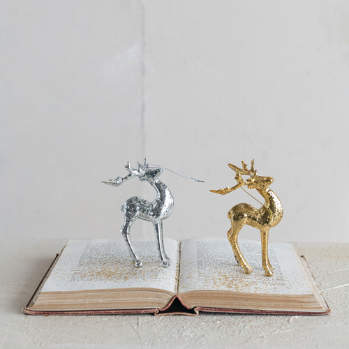 Silver and gold metallic deer ornaments  on an open book, on a white surface.  Against a light gray background.