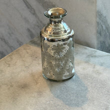Load image into Gallery viewer, Silver Mercury Glass Etched Bud Vase, cylindrical silver mercury glass etched bud vase with subtle floral detailing and a narrow flanged neck, displayed on a light stone surface against a gray marble background. 