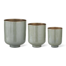 Load image into Gallery viewer, Sage Green Metal Footed Nesting Pots Set, trio of sage green enamel-finish metal nesting pots with warm metallic interiors and top rims, sturdy footed bases, and graduating sizes, displayed against a white background. 